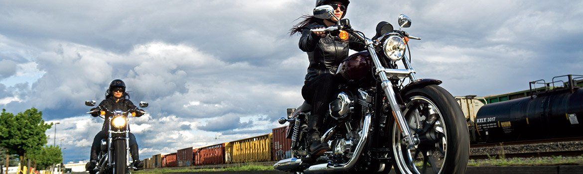 Two women ride motorcycles while racing a train.