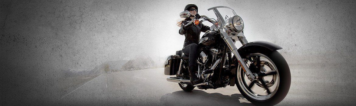 Woman with long hair and dark glasses rides a shiny motorcycle.