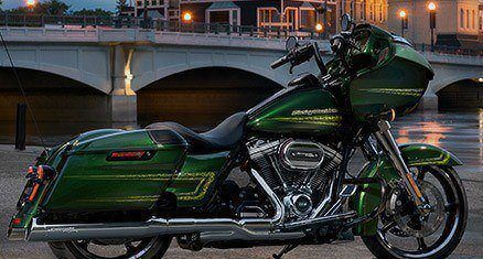 A green motorcycle parked before a river bridge.